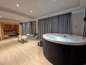 Un moderno cuarto de spa con bañera de hidromasaje, zona de estar y sauna de madera.