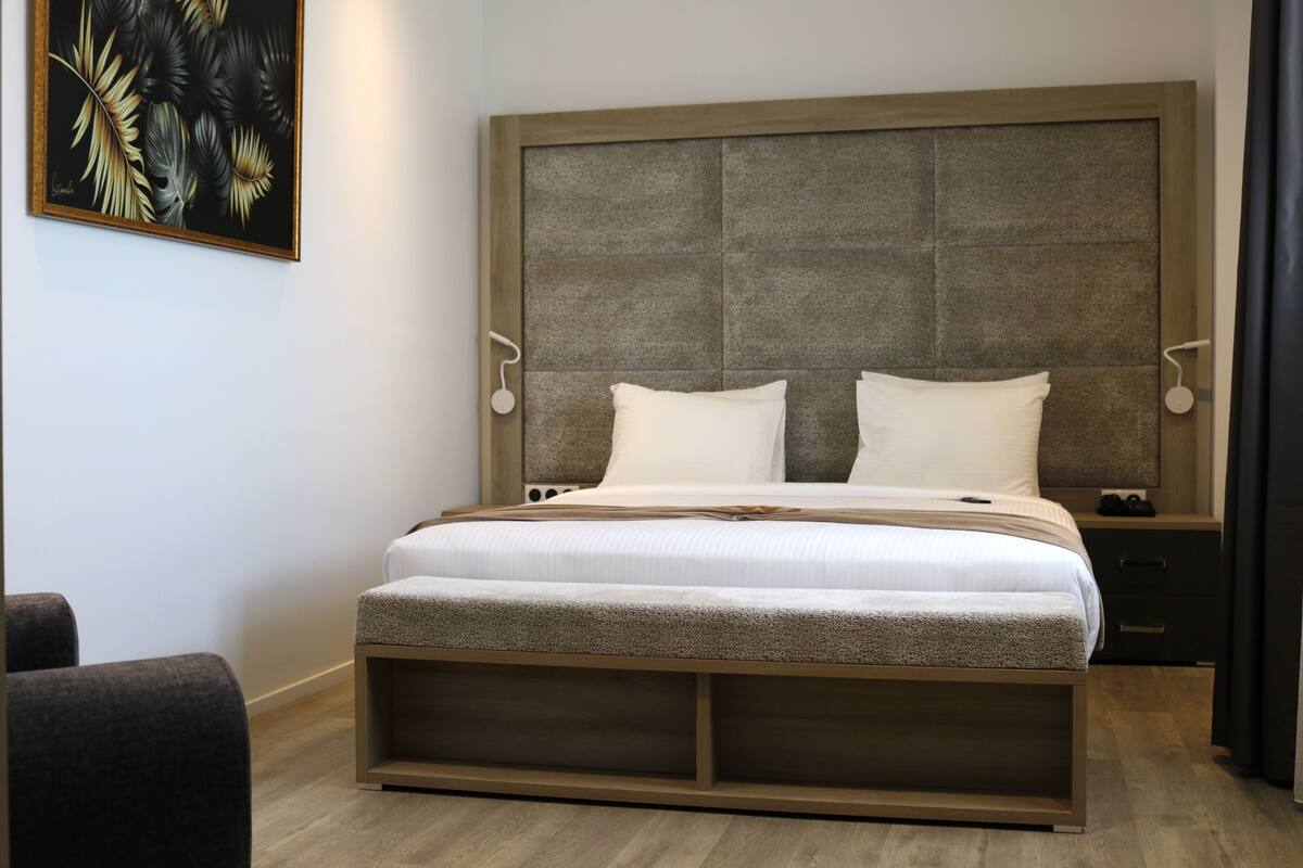 A modern bedroom with a large bed, a headboard with a textured panel, bedside tables, and a wall-mounted artwork.
