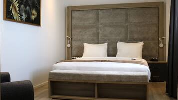 Un dormitorio moderno con una cama grande, cabecera con panel texturizado, mesitas de noche y una obra de arte colgada en la pared.