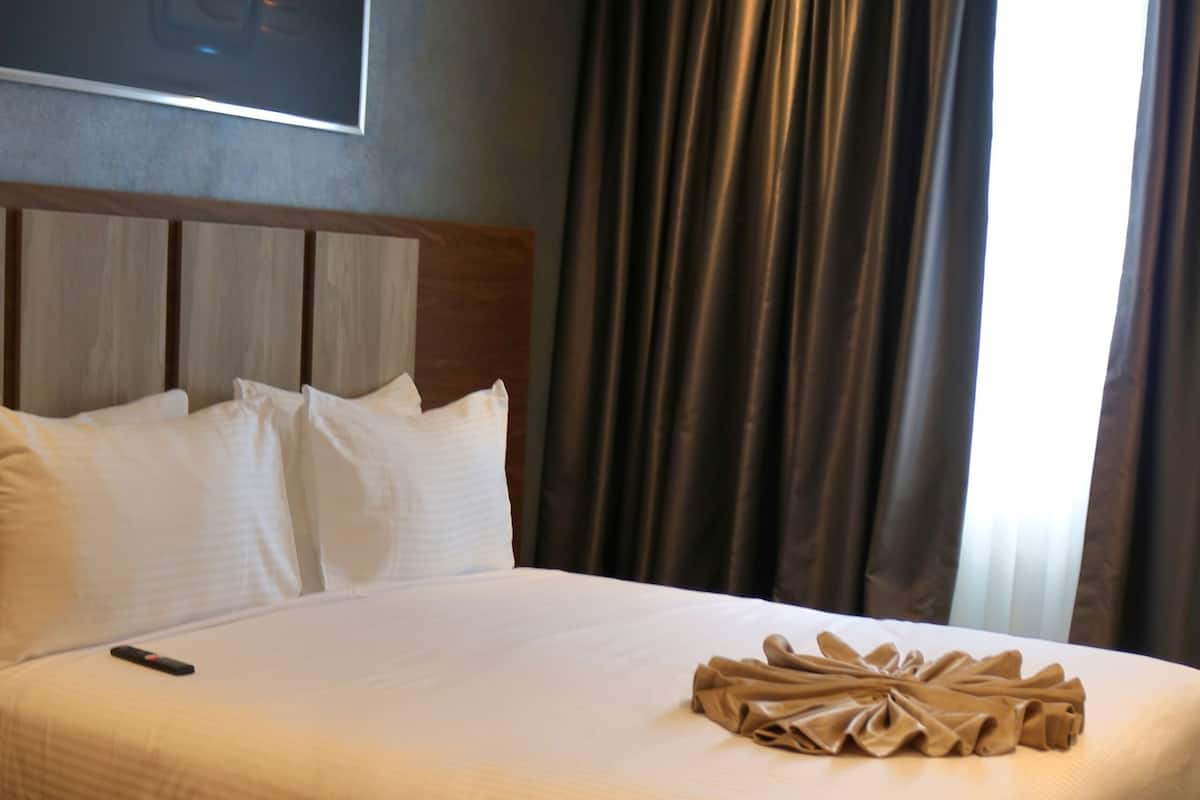A neatly made bed with white linens, a remote control on the bed, and a decorative towel on the footboard.