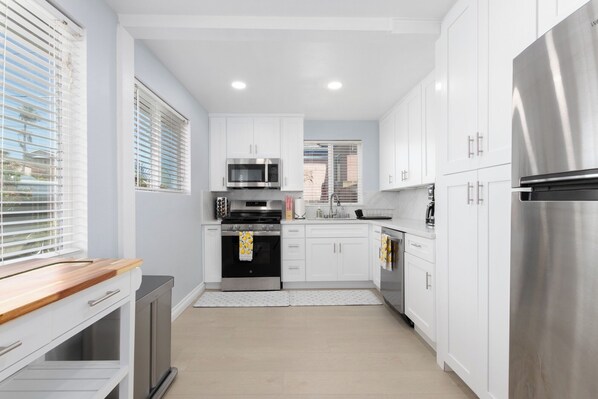 A modern kitchen with white cabinets, stainless steel appliances, and a wooden countertop.