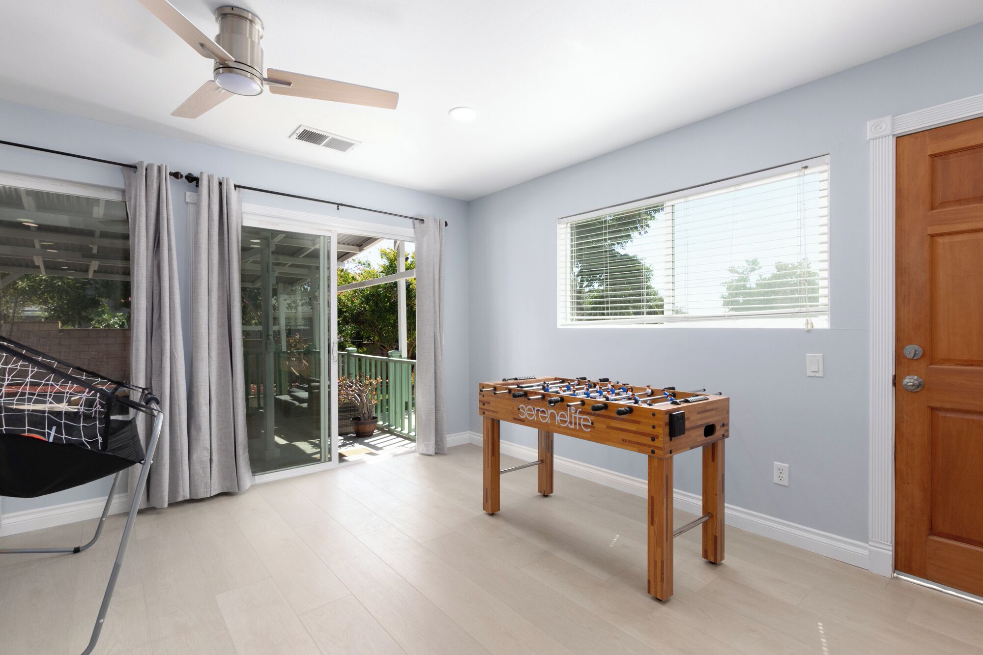 A room with a foosball table, a ceiling fan, and a view through a sliding glass door to an outdoor area.
