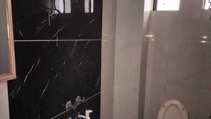 Une salle de bain avec un mur en marbre noir, des toilettes blanches et un seau bleu posé sur le sol.