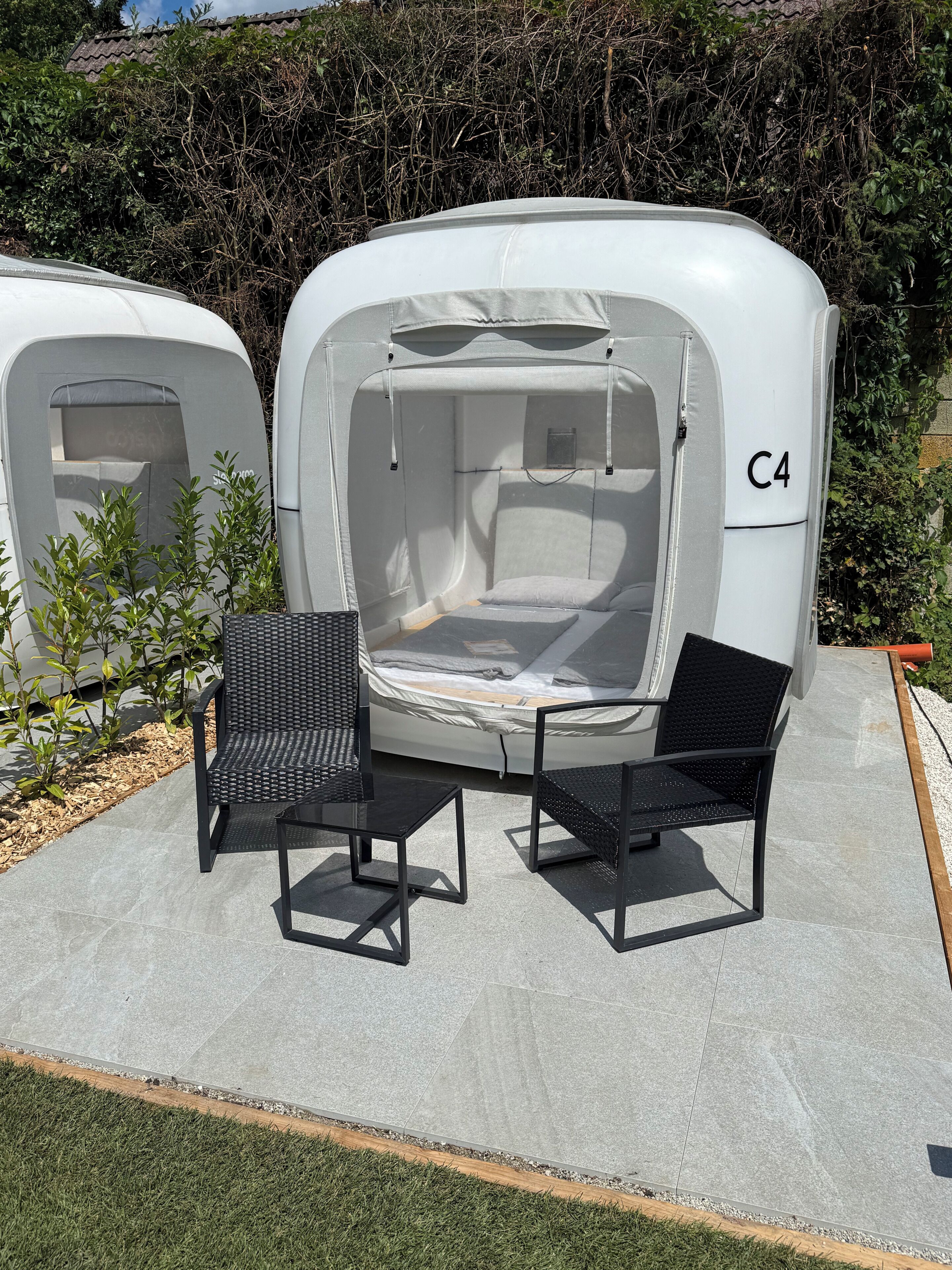 Un espace extérieur abrité avec deux chaises et une table, une tente comprenant un espace pour dormir et une petite fenêtre.