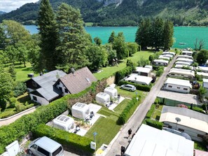 Un terrain de camping avec plusieurs caravanes, une petite maison et un lac en arrière-plan.