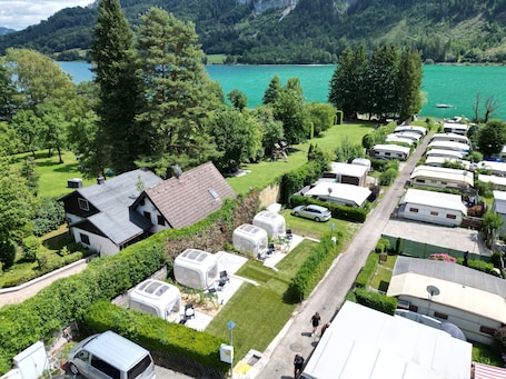 A caravan park with multiple caravans, a small house, and a lake in the background.