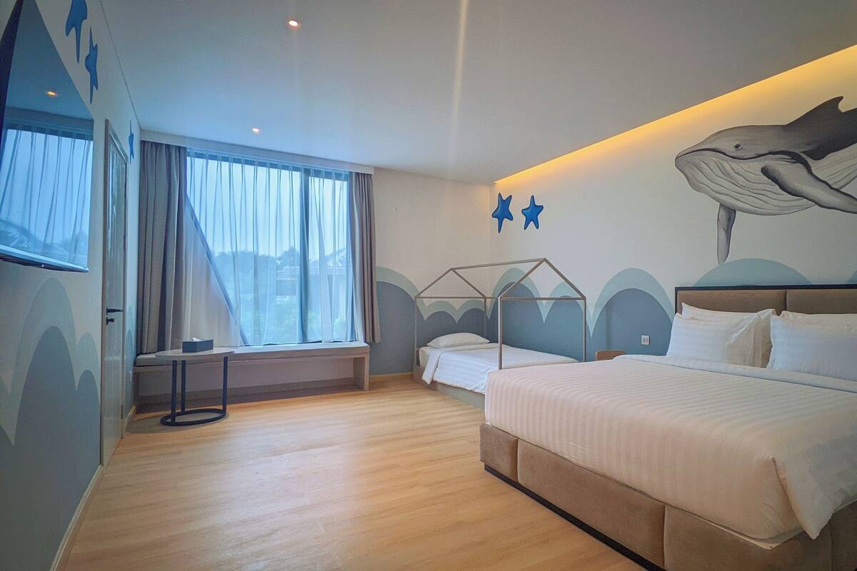 A hotel room with a large bed, a window with curtains, a wall mural, and a small table.