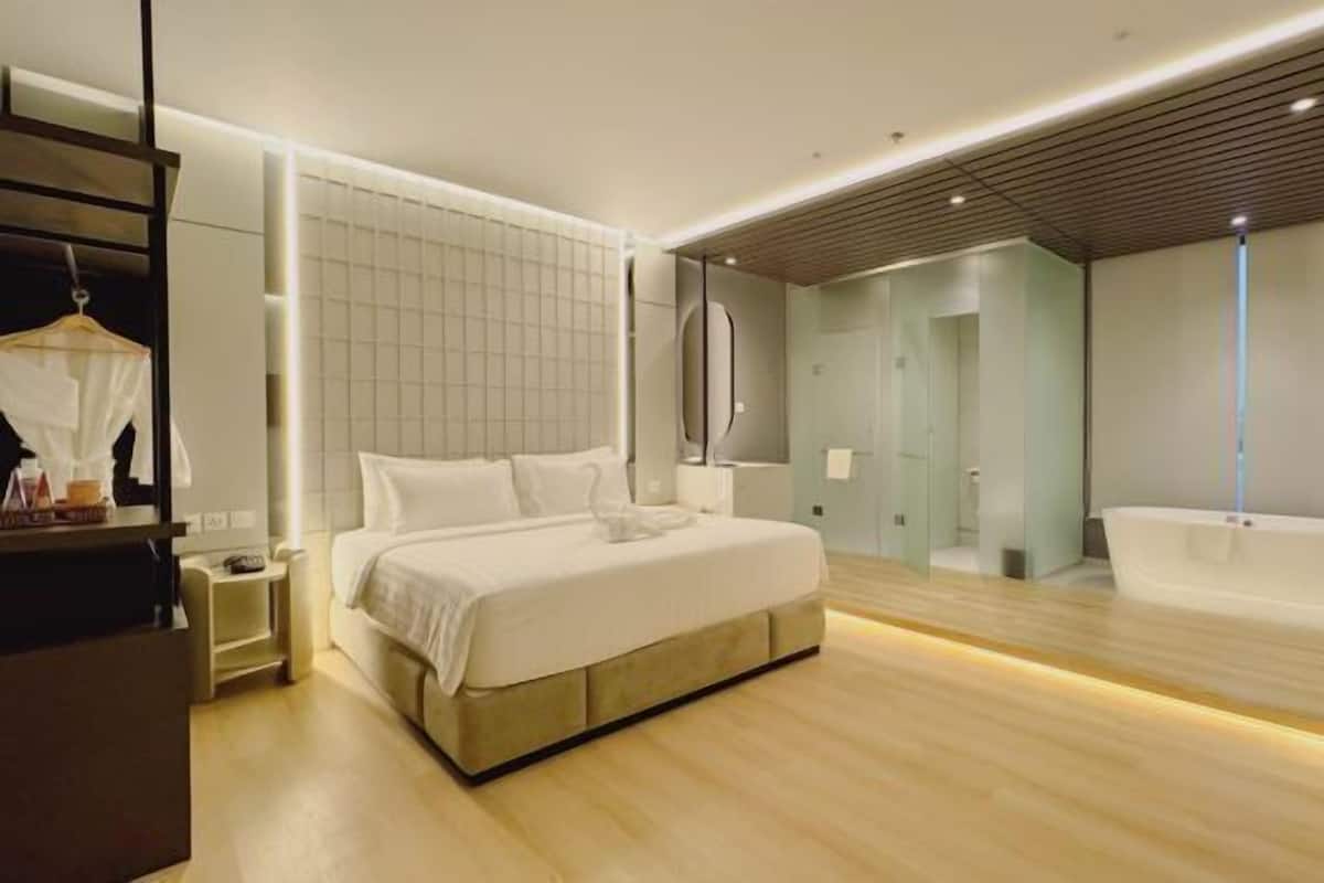 A modern bedroom with a large bed, a walk-in closet, a bathroom with a bathtub, and a large mirror.