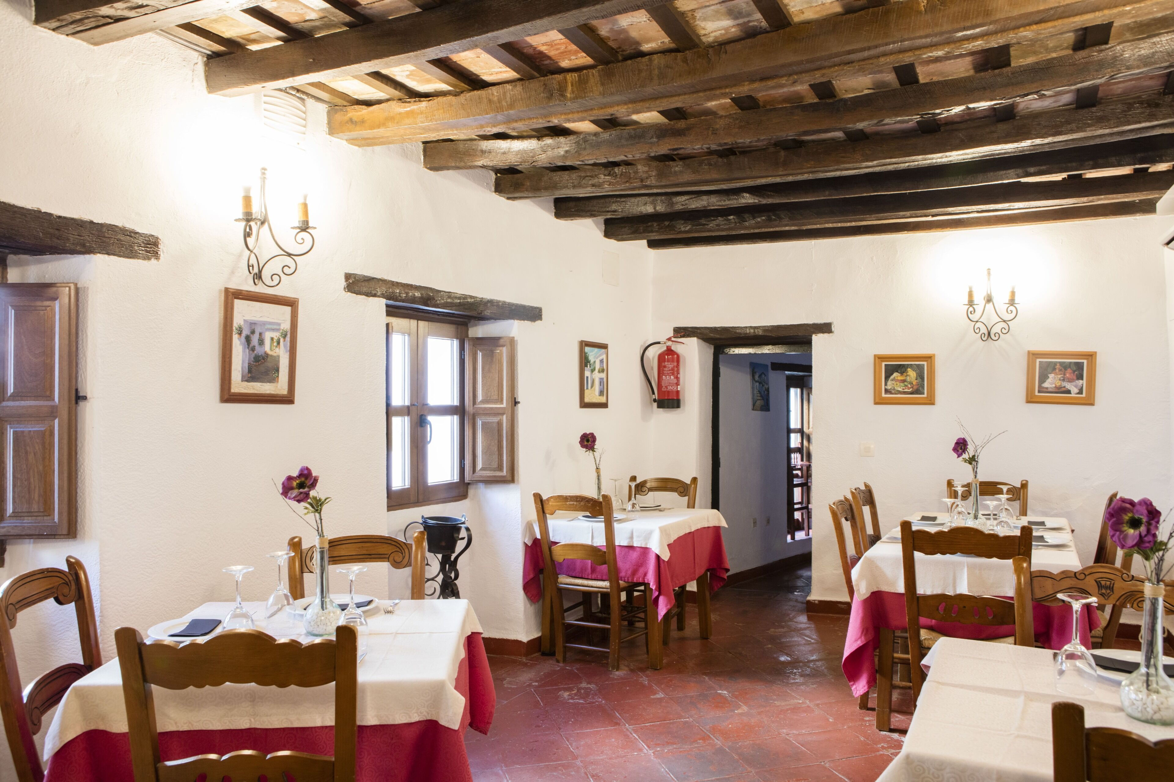 Un espace repas agrémenté de poutres en bois, de murs blancs et de tables recouvertes de nappes rouges et blanches.