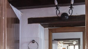 Un baño con pared de azulejos blancos, un taburete de madera con una toalla, un lavamanos y un espejo.