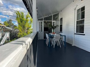 A covered porch with a dining table and chairs, a railing, and a view of the outdoors.