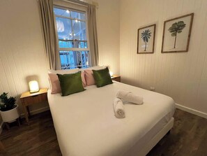 A neatly made bed with pillows, a bedside lamp, and a window with curtains.