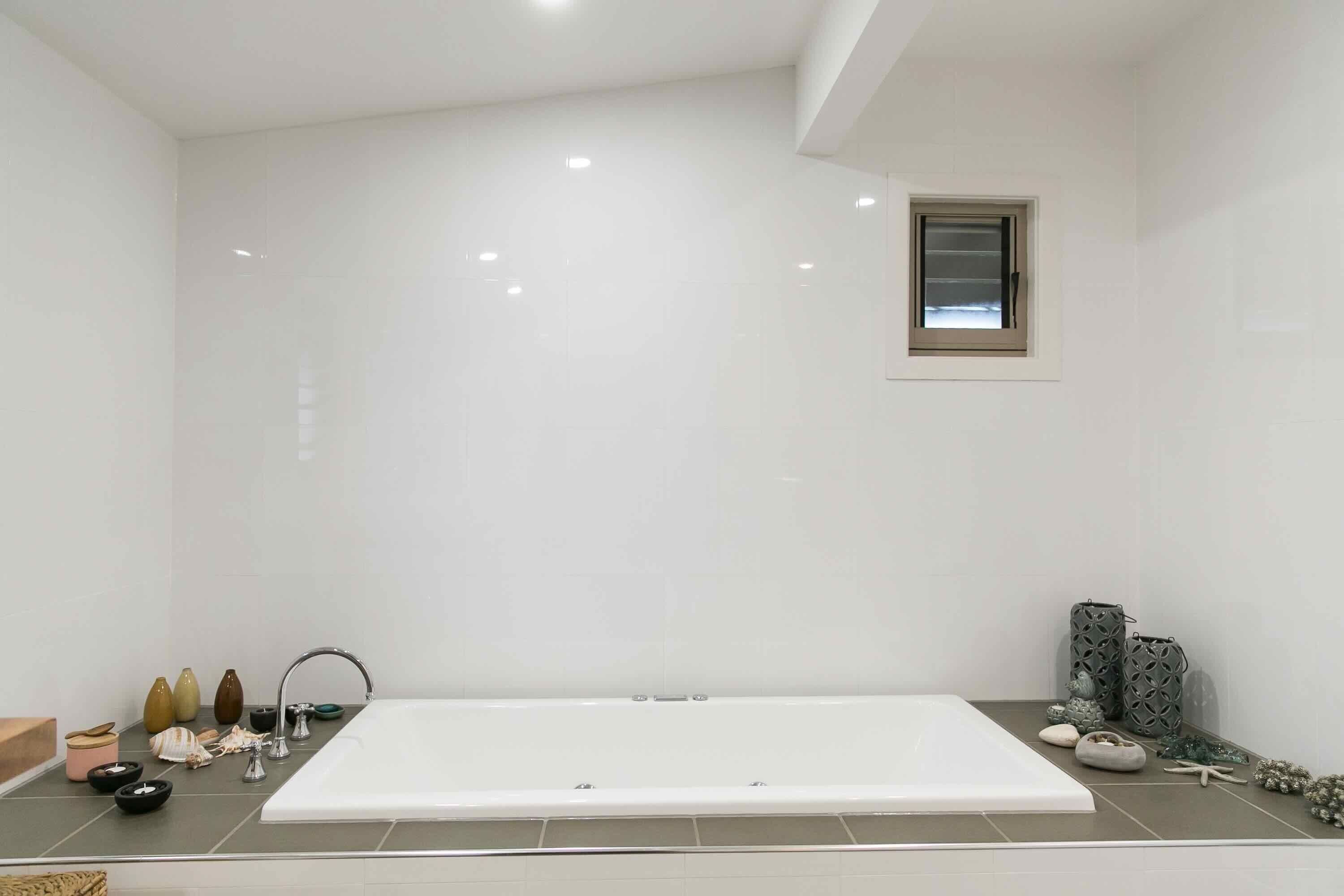 Un baño moderno con una bañera blanca grande, una ventana pequeña y diversos artículos de aseo en la encimera.