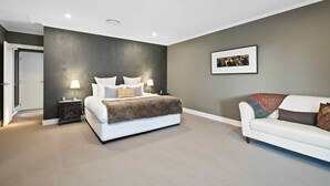 Une chambre à coucher avec un lit, des tables de chevet, un canapé blanc et un tableau encadré au mur.