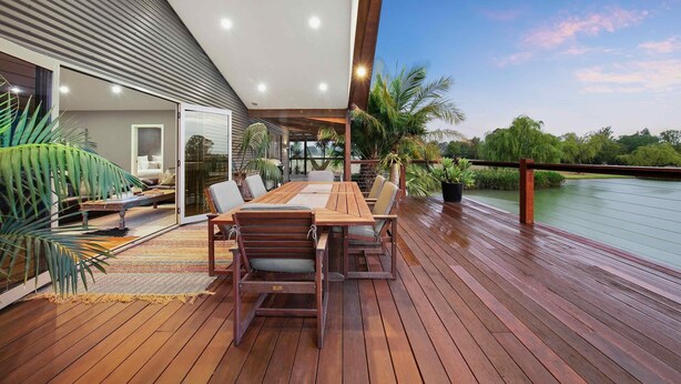 Une terrasse en bois avec une table et des chaises, donnant sur une étendue d’eau.