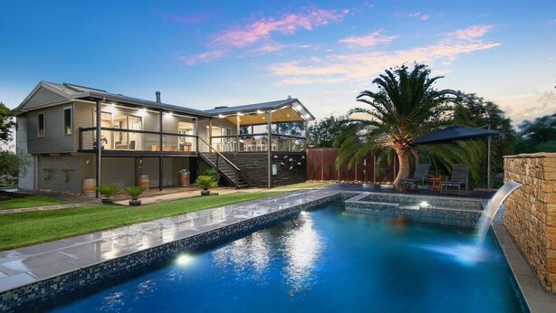Una casa moderna de dos pisos con piscina, mobiliario exterior y un césped bien cuidado.