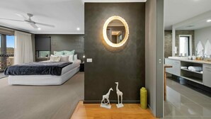 Un dormitorio moderno con cama, ventilador de techo, espejo grande y lámpara circular fijada a la pared.