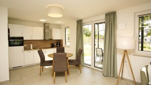 A modern kitchen with white cabinets, a dining table with chairs, and a large window with curtains. - Beachfront vacation rental with a terrace, access to the pool and sauna - Rex Rugia (Mönchgut OT Lobbe)
