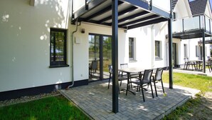 A modern outdoor patio area with a table and chairs, a covered seating area, and a glass door leading to an indoor space. - Beachfront vacation rental with a terrace, access to the pool and sauna - Rex Rugia (Mönchgut OT Lobbe)