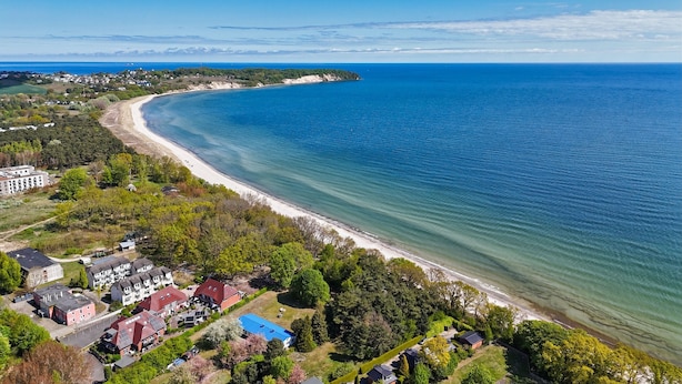 An aerial view of a coastal area with a beach, residential buildings, and a clear blue sky. - Beachfront vacation rental with a terrace, access to the pool and sauna - Rex Rugia (Mönchgut OT Lobbe)
