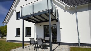 A modern house with a covered patio area, a built-in table and chairs, and a large window.