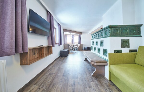 A modern living room with a flat-screen TV, wooden flooring, a green sofa, and a dining area with a table and chairs. - Chalet Fabian by we rent (Saalbach)