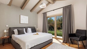 A bedroom with a bed, a chair, a nightstand, a lamp, and a window with curtains.