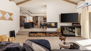 A modern living room with a sofa, a coffee table, and a TV. There is a kitchen in the background with a dining area.