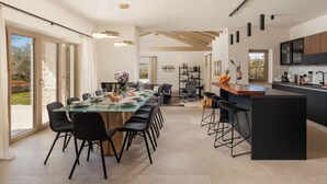 A modern kitchen with a central island, a dining area with a glass table, and a view of the outdoors.