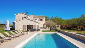 A stone villa with a swimming pool, outdoor furniture, and a clear blue sky.