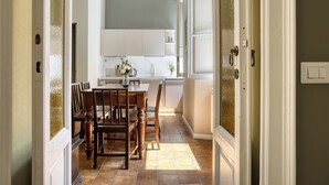 Un coin repas avec une table et des chaises en bois, une cuisine à l’arrière-plan et une vue à travers une porte.