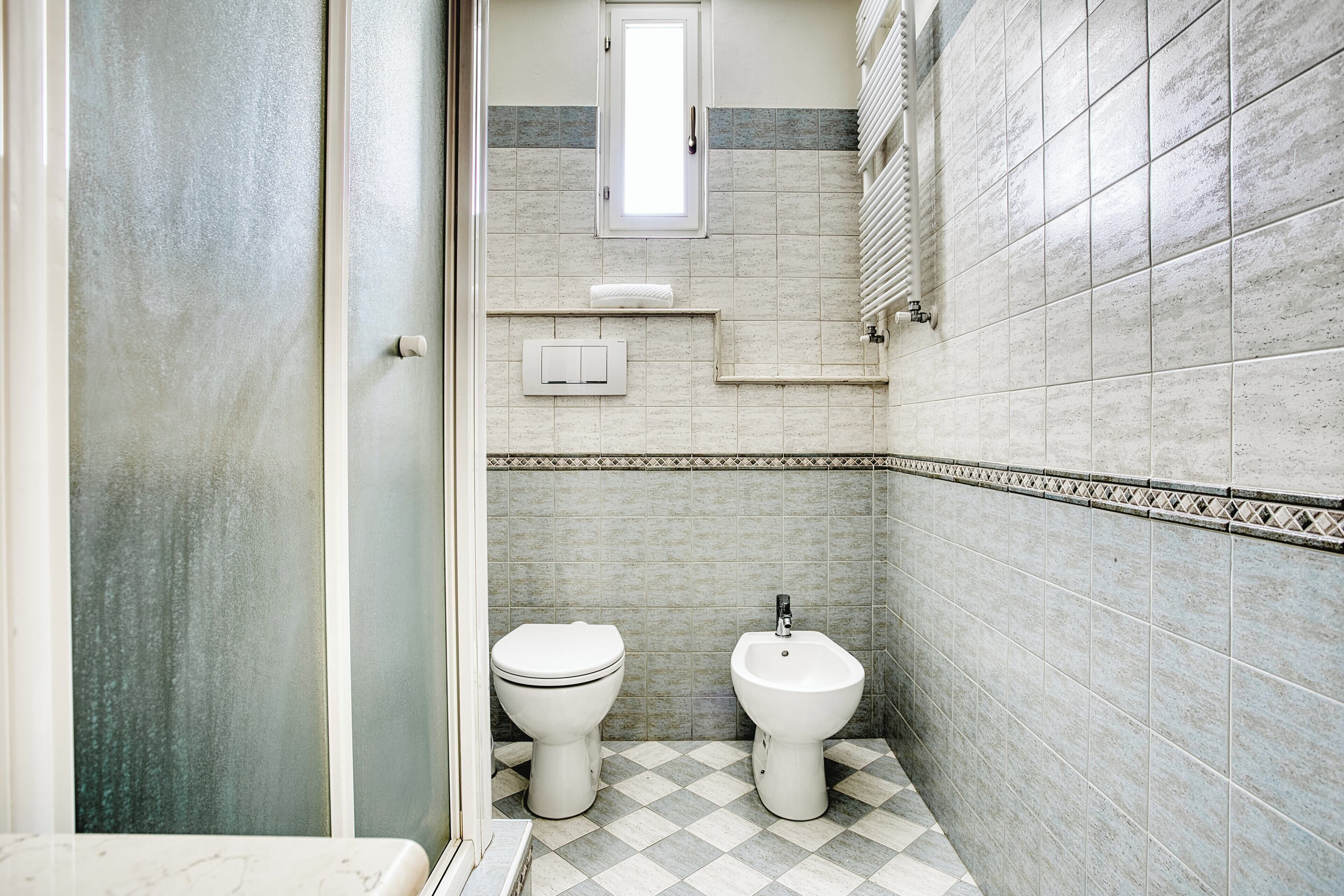 A bathroom with a toilet, bidet, and a small window.