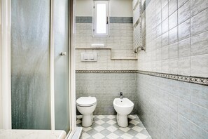 Een badkamer met toilet, bidet en een klein raam.