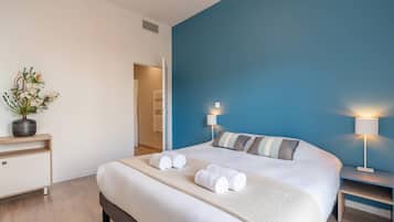 Una habitación de hotel moderna con una cama grande, dos lámparas de noche, una mesita de noche, una planta en maceta y vistas al pasillo.