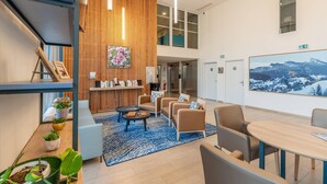 Een moderne lobby met een houten receptiebalie, een zithoek en een groot schilderij aan de muur.