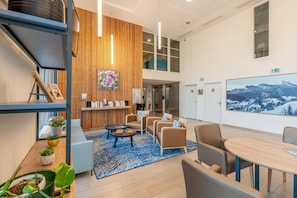 Een moderne lobby met een houten receptiebalie, een zithoek en een groot schilderij aan de muur.