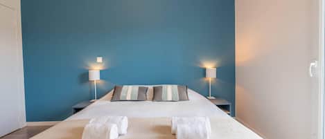 A hotel room with a large bed, two bedside lamps, and a view of the outside.
