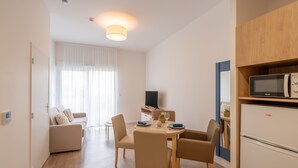 Een moderne woonkamer met een bank, eettafel en stoelen. Er staat een televisie op een dressoir en een koelkast met een magnetron.