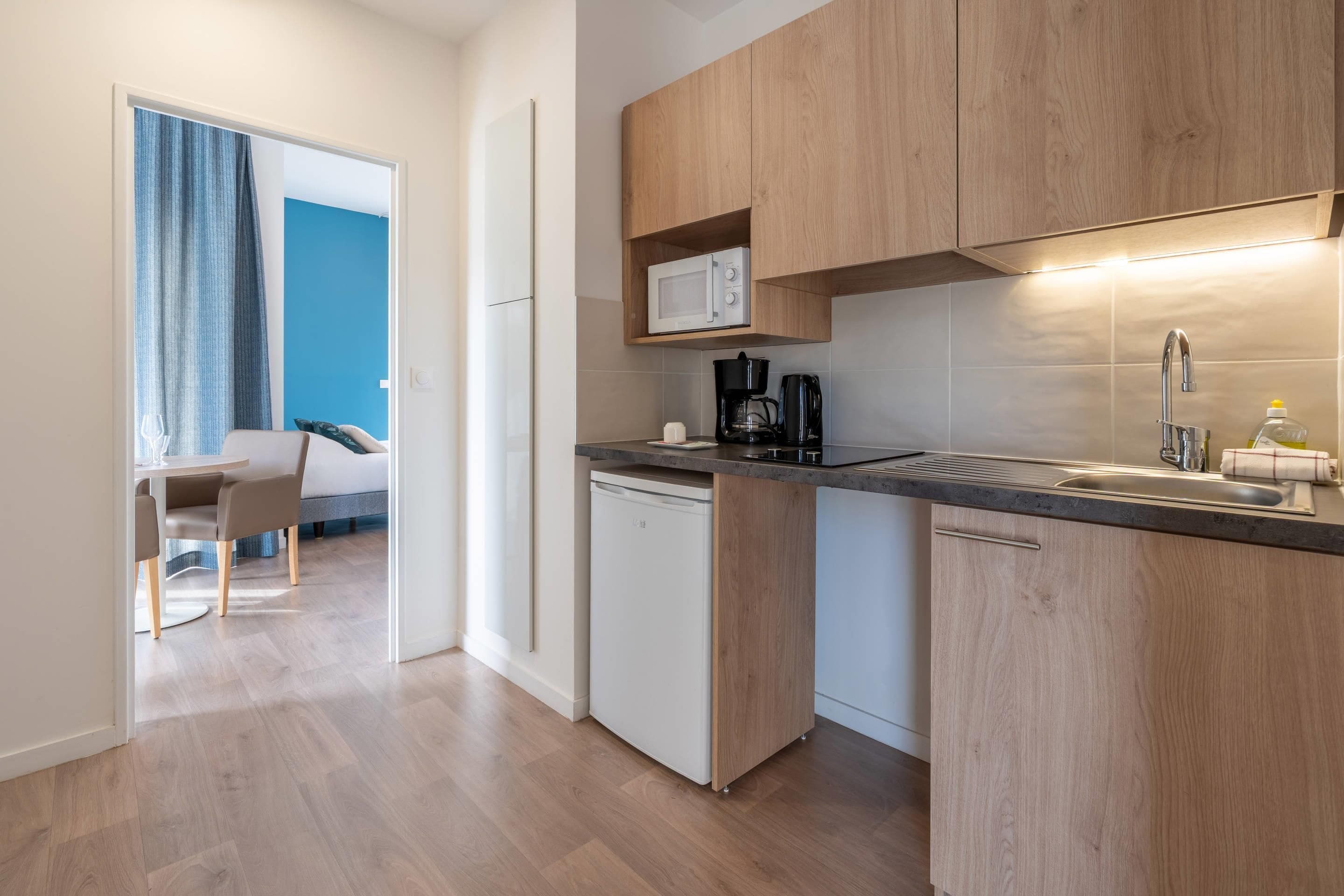 A compact kitchen with wooden cabinets, a microwave, a coffee maker, and a dishwasher.