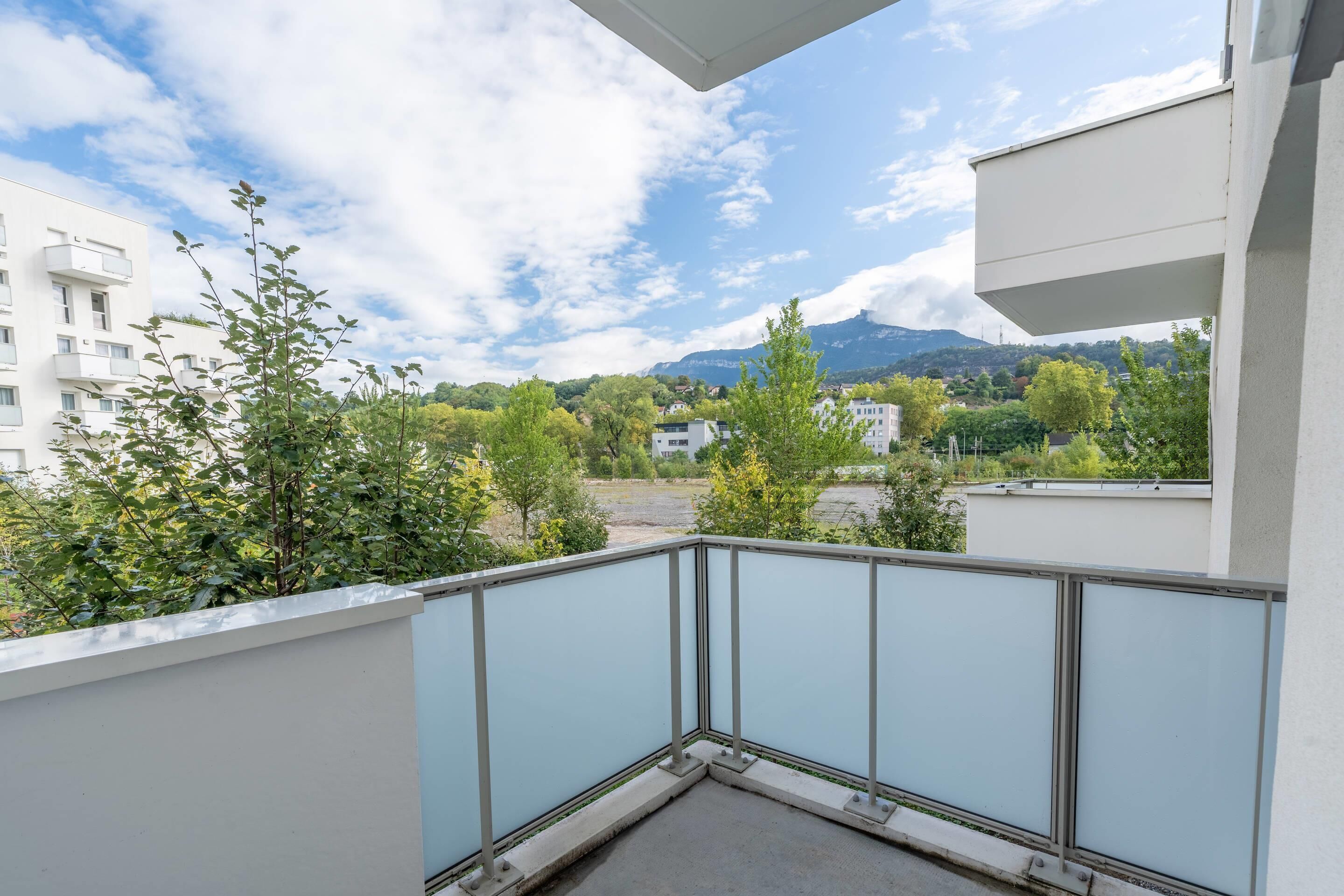 A balcony with a metal railing, overlooking a residential area with trees and buildings.