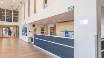 Un hall d’entrée spacieux avec un comptoir de réception, un plancher en bois et une vue sur l’intérieur grâce à de grandes fenêtres.