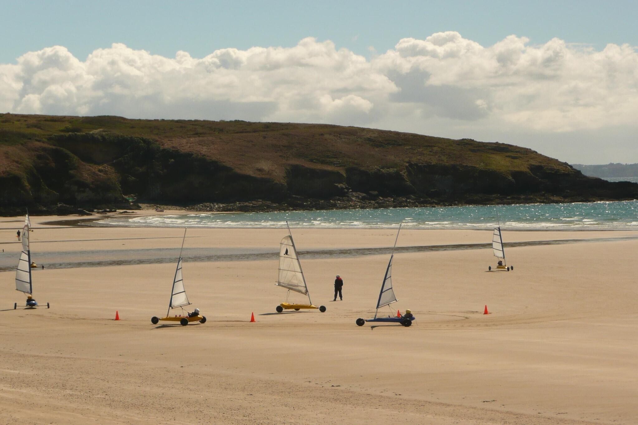 A beach with three sailboats and a person standing on the sand.