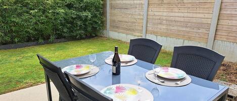 A rectangular outdoor table set for four with black chairs, a bottle, and plates with a colorful design.