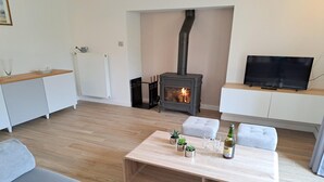 Una sala de estar moderna con chimenea, un sofá, una mesa de centro con plantas y vasos, y un televisor sobre un mueble.