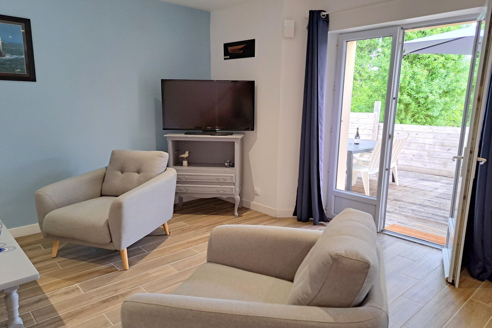 A living room with a television on a stand, two sofas, a small table, and a sliding glass door leading to an outdoor area with a table and chairs.