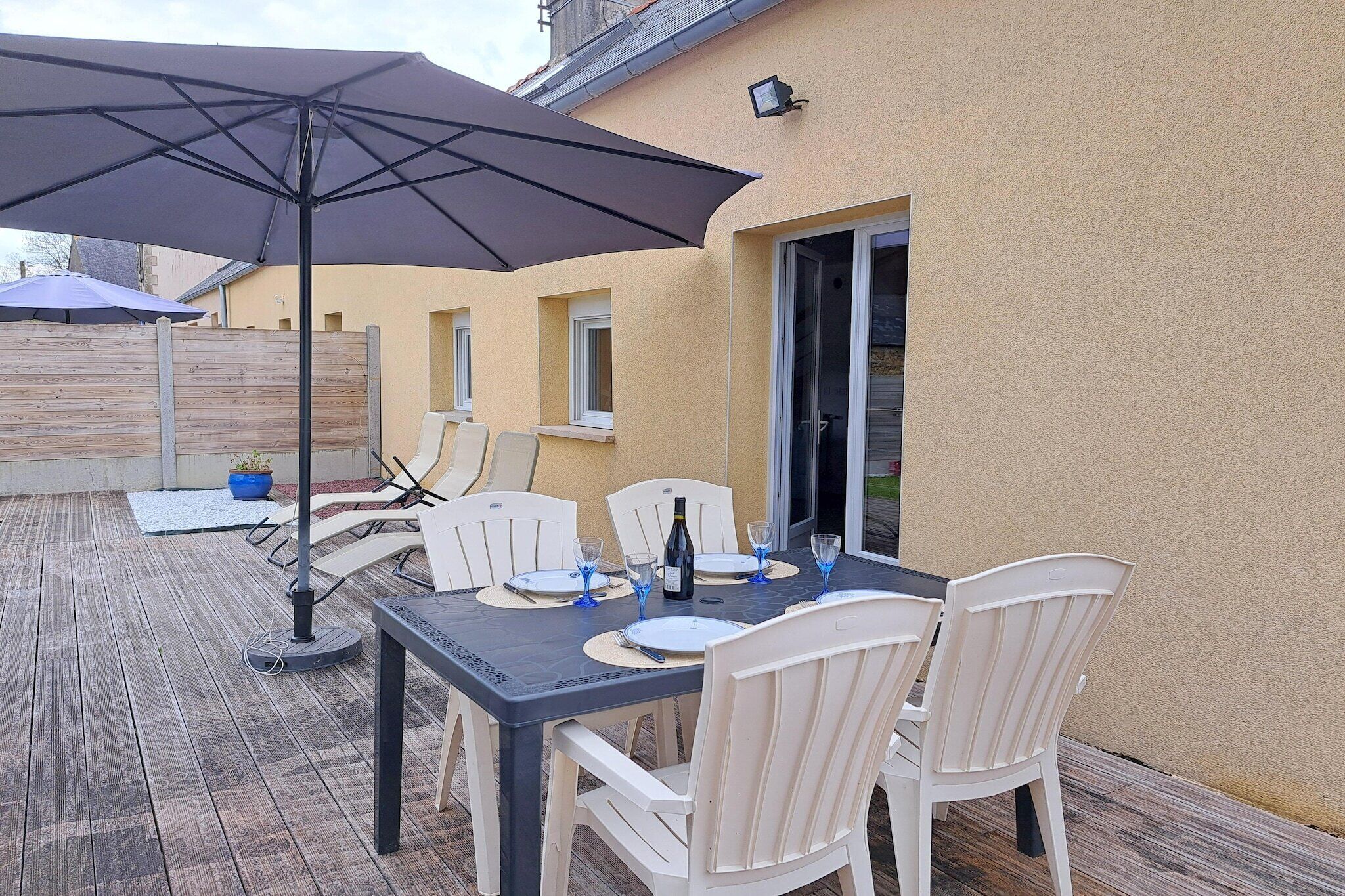 An outdoor patio with a table set for four, a large umbrella, and a wooden deck.