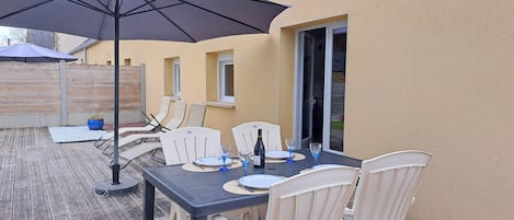 An outdoor patio with a table set for four, a large umbrella, and a wooden deck.