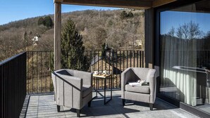 A balcony with two grey armchairs and a small table, overlooking a forested hillside. - Villa in Belgium with Private Terrace (La Roche-en-Ardenne)