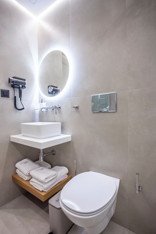 Un baño moderno con lavamanos, espejo e inodoro blancos.