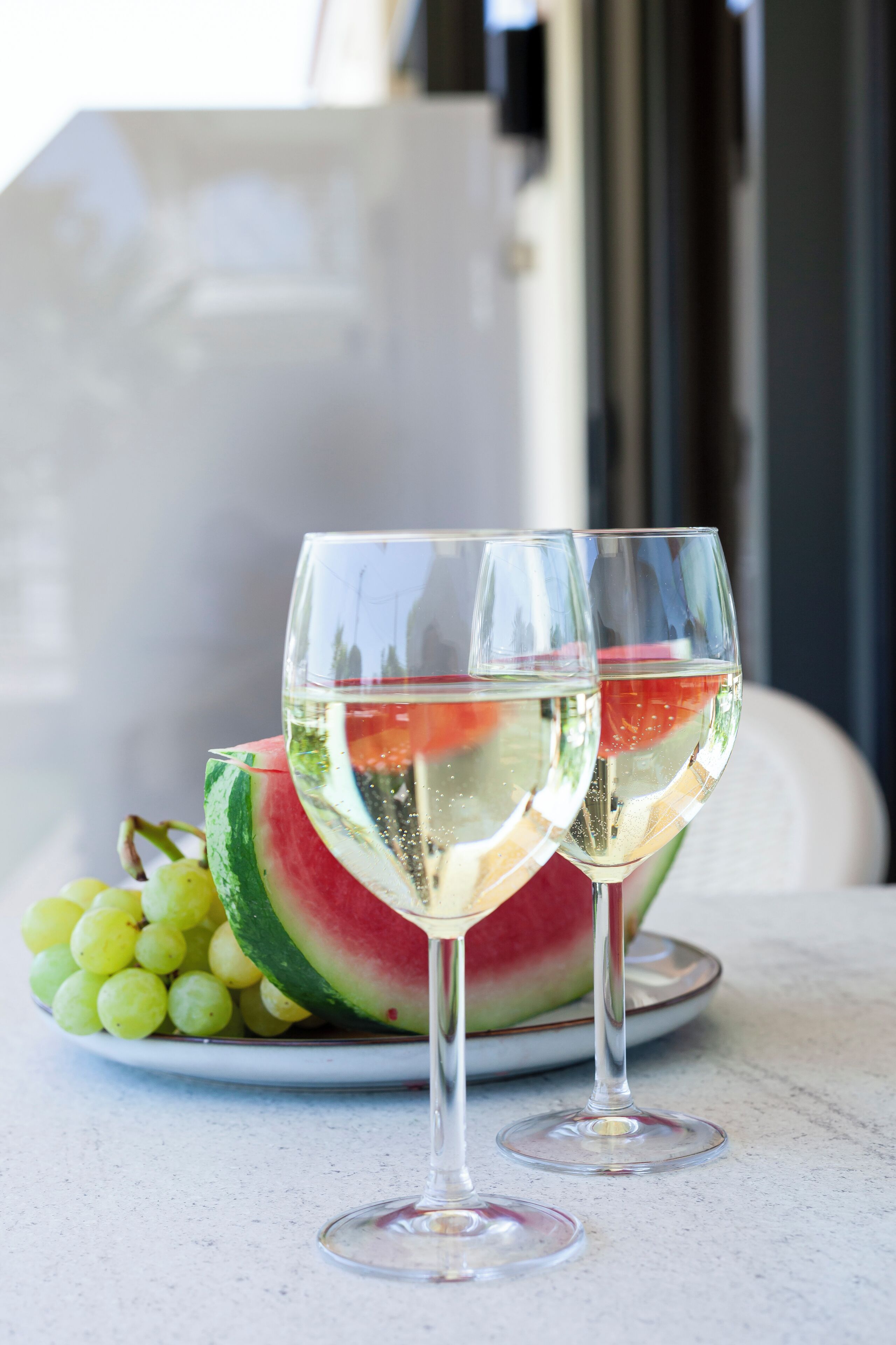 Two wine glasses with a watermelon slice and grapes on a plate.